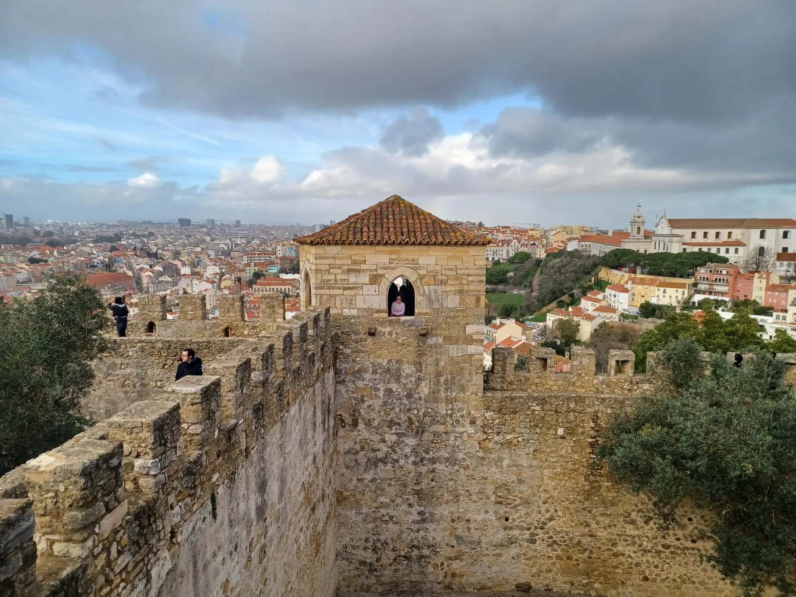 The walkable stone ramparts of São Jorge castle in Lisbon, with a square watchtower and the city's rooftops spread out below