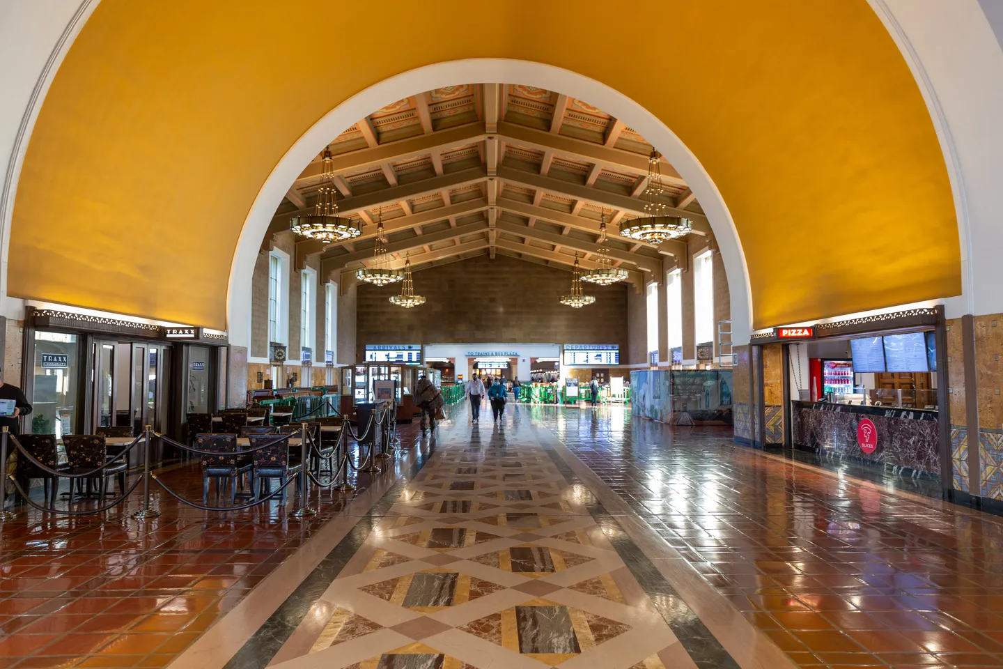 The main hall of Los Angeles Union Station, a tall arched space with a beamed wooden ceiling, ochre walls, hanging Art Deco chandeliers and a patterned inlaid marble floor running away from the camera