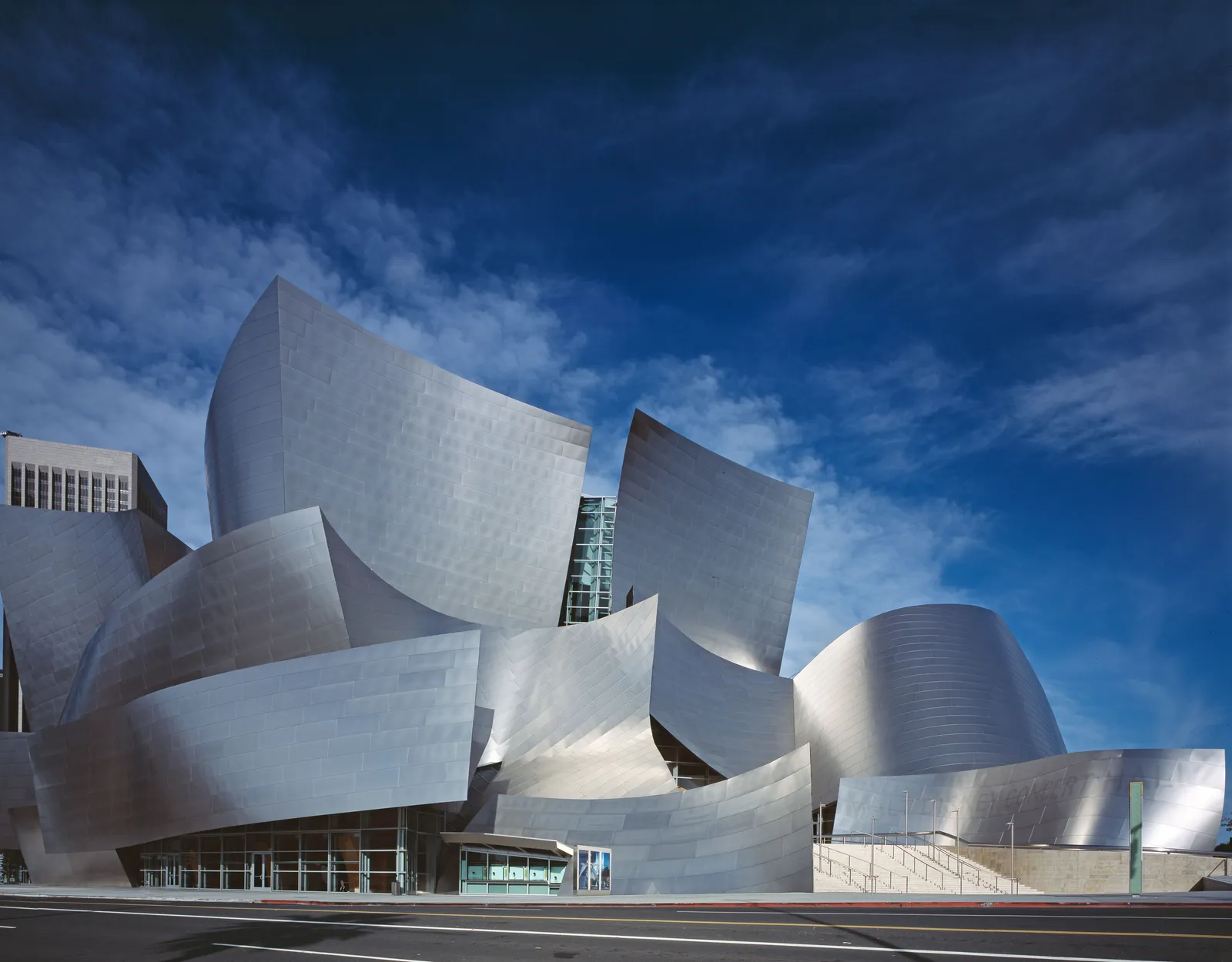 Walt Disney Concert Hall in Los Angeles seen from the street, its curved stainless steel panels folding over each other like sails against a blue sky
