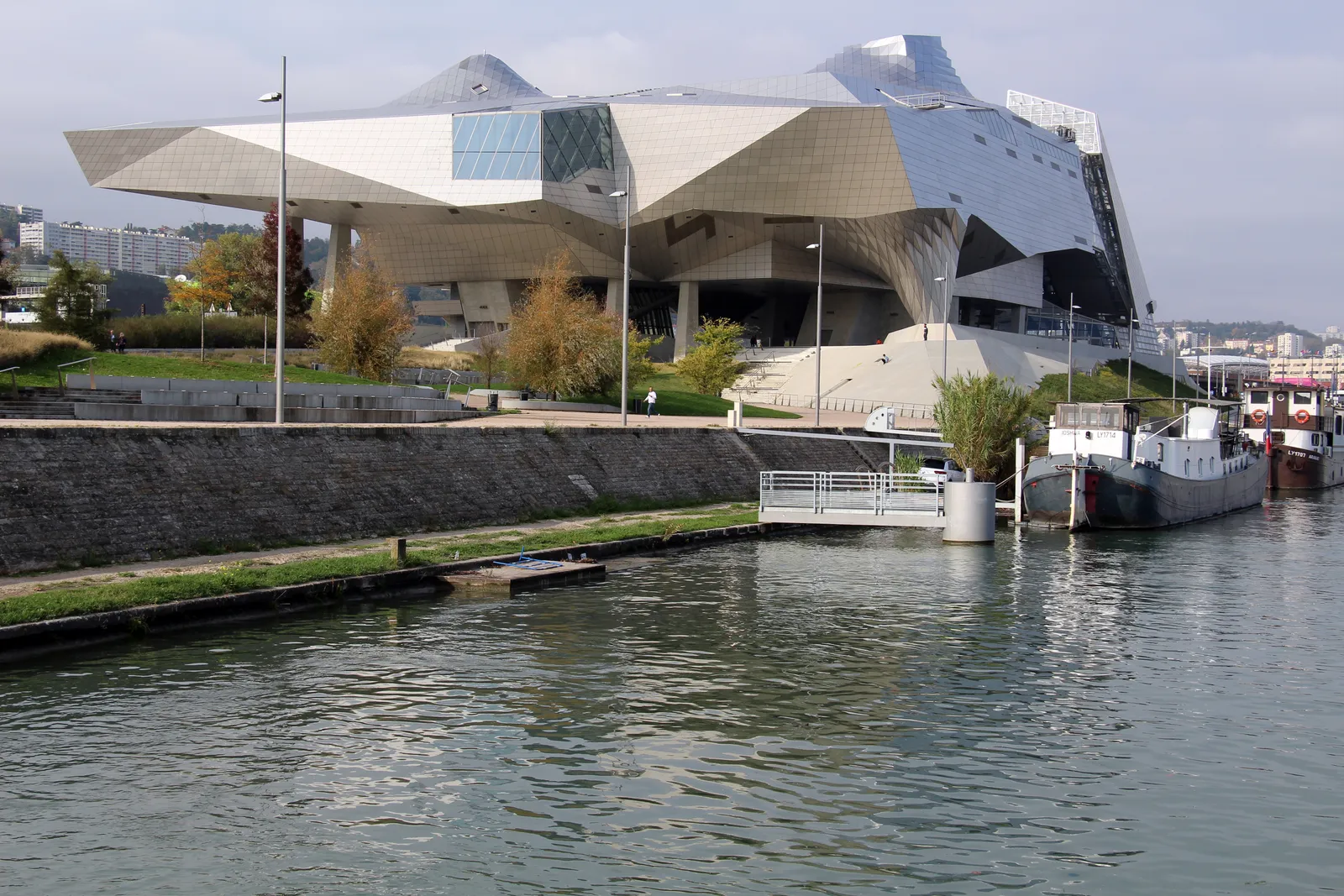 The Musée des Confluences in Lyon seen across the water, an angular building of stainless steel and glass raised on concrete supports at the riverside