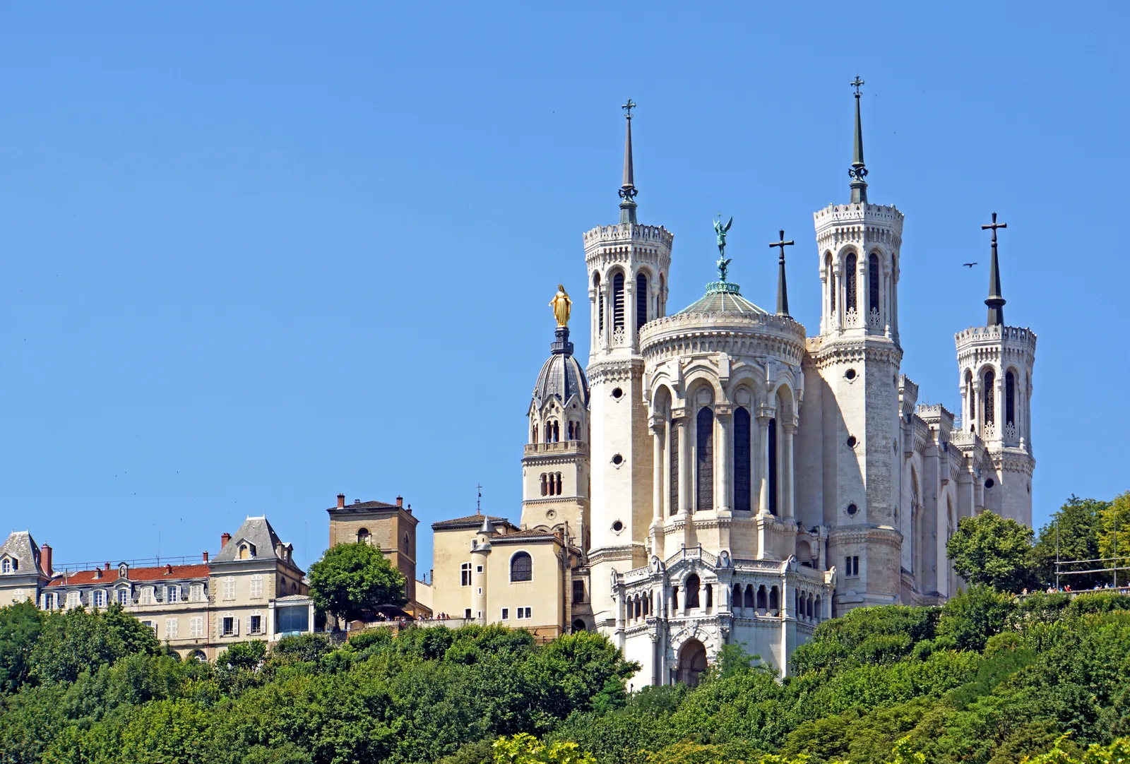 The Basilica of Notre-Dame de Fourvière on its hilltop in Lyon, a white stone church with four corner towers and a gilded statue of the Virgin on a smaller belfry beside it