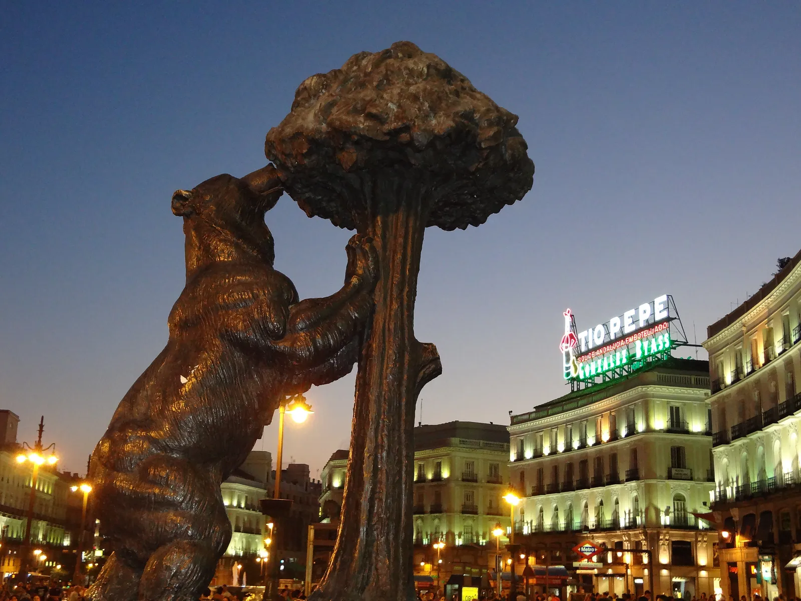 The bronze bear and strawberry tree statue in Puerta del Sol, with the lit Tio Pepe sign behind it