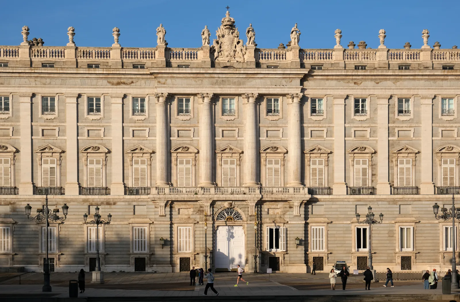 The pale stone facade of Madrid's Royal Palace seen across the open plaza in front