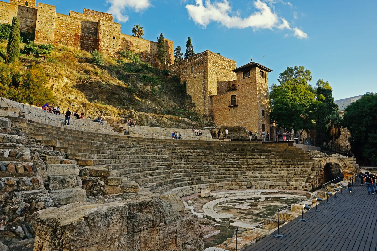 The tiered stone seating of Málaga's Roman Theatre with the Alcazaba's walls rising behind it