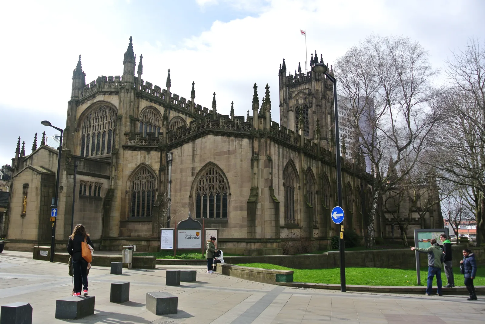Manchester Cathedral's tower and stone facade on Victoria Street, with the city skyline visible behind it