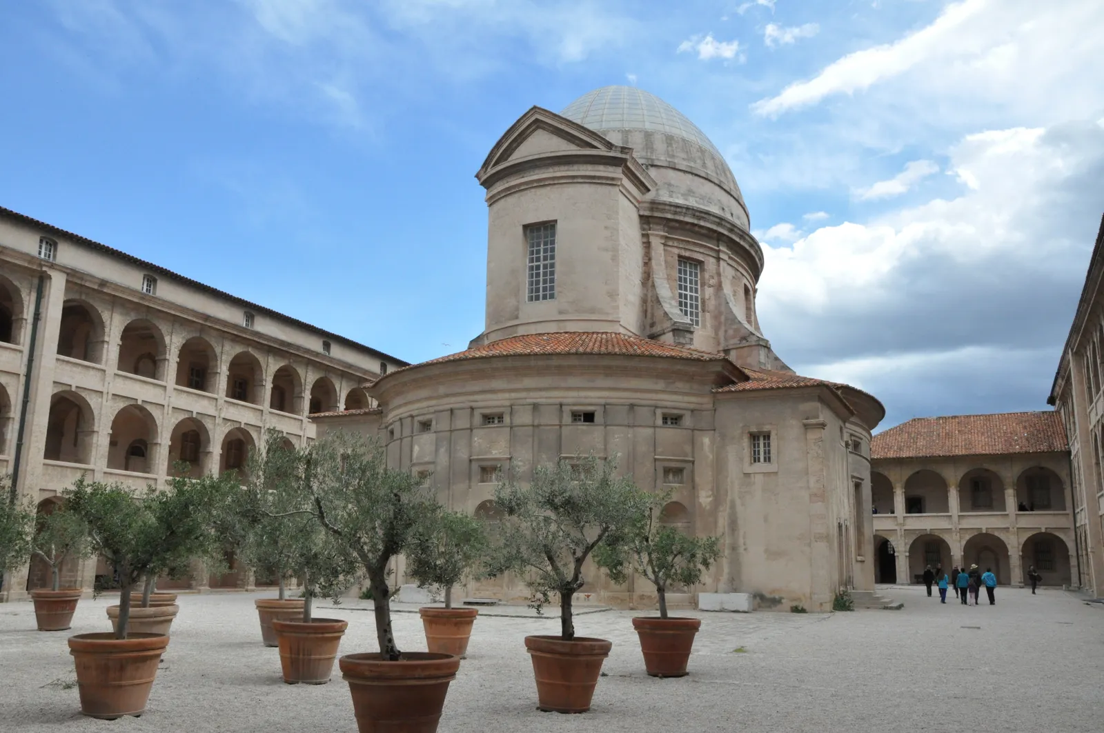 The domed central chapel of La Vieille Charité in Marseille's Le Panier district, seen across its courtyard lined with potted olive trees and three-storey arcaded galleries
