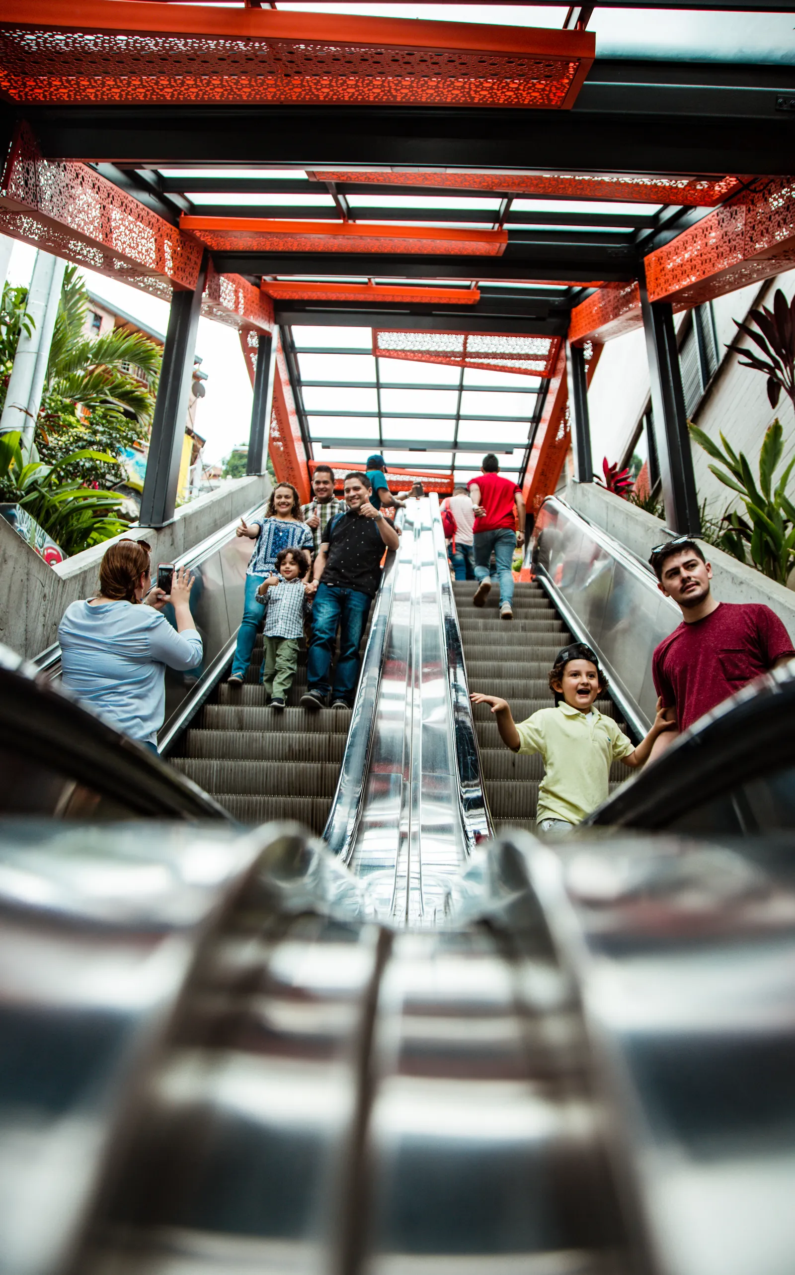 Families riding one of Comuna 13's six orange-canopied outdoor escalators up the hillside, with murals painted along the walls beside the steps
