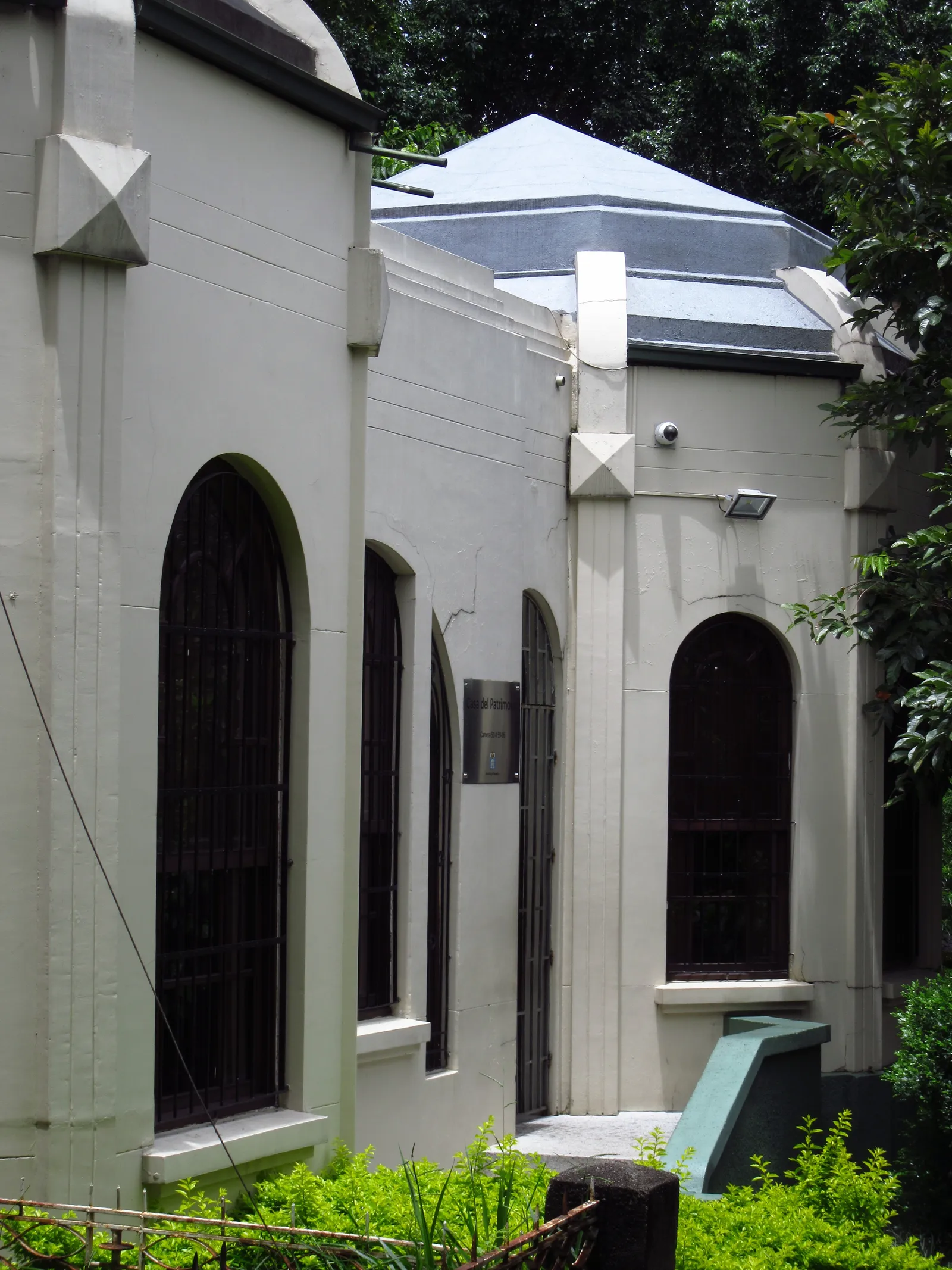 A weathered two-story art deco house on a residential street in Medellín's Prado neighborhood, with a motorcycle parked in front