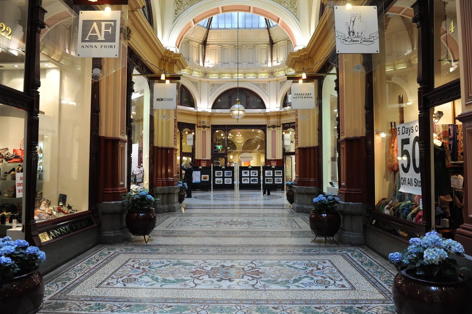 The interior of the Block Arcade in Melbourne, its patterned mosaic tile floor running the length of the arcade between shopfronts toward a lit glass dome
