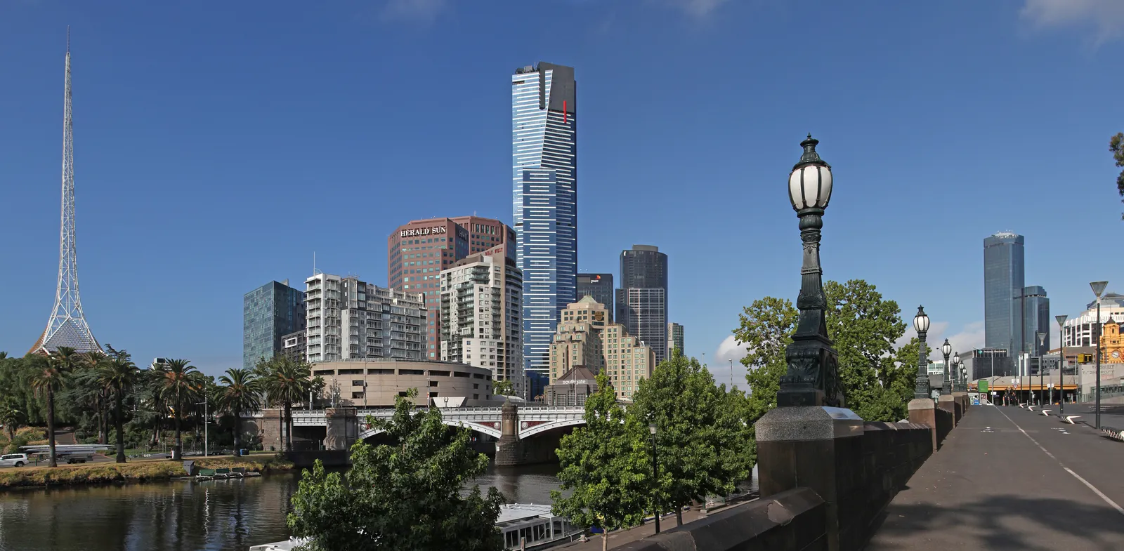 Eureka Tower rising above the Southbank riverfront in Melbourne, seen from the Yarra embankment with Princes Bridge and the spire of the Arts Centre to the left