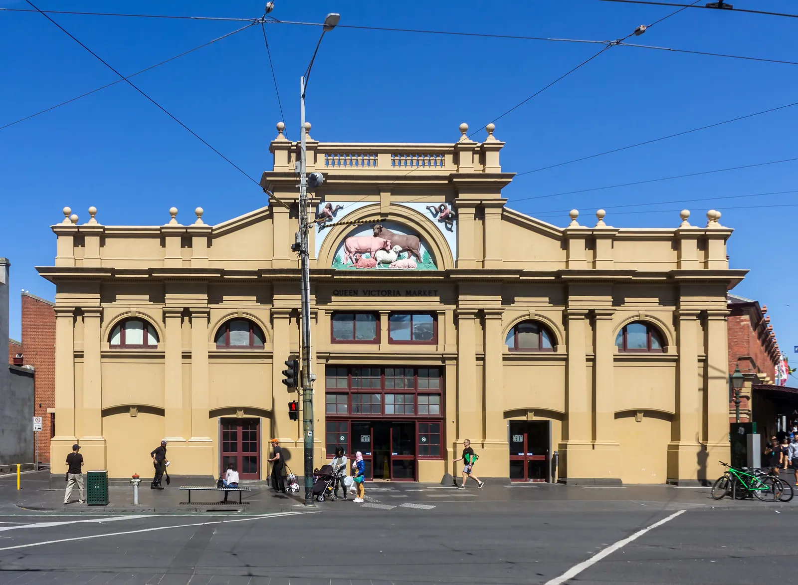 The Elizabeth Street frontage of Queen Victoria Market in Melbourne, a cream nineteenth-century facade with arched windows and a painted lunette above the entrance