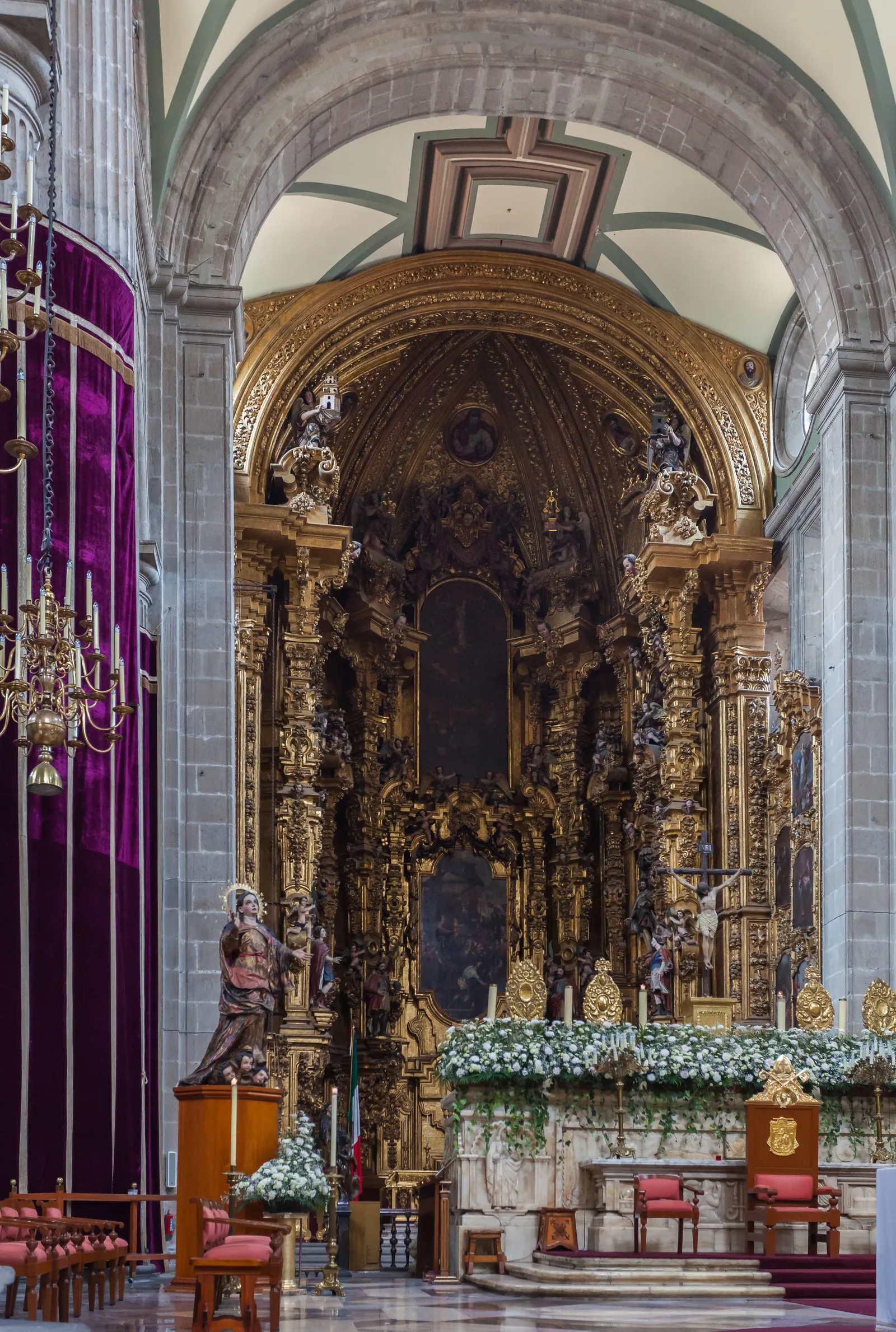 The gilded Altar de los Reyes inside Mexico City's Metropolitan Cathedral, a towering carved and gold-leafed wooden altarpiece set under a stone arch, with candles and flowers at its base