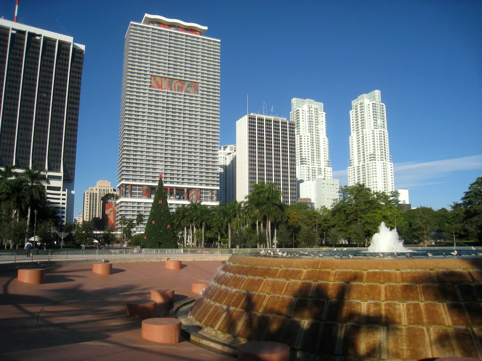 A stepped circular fountain on a paved plaza in Bayfront Park, Miami, with palm trees and downtown high-rises along Biscayne Boulevard behind it