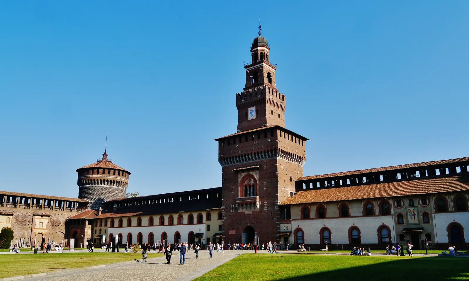 The brick tower and courtyard of Castello Sforzesco in Milan under a clear blue sky