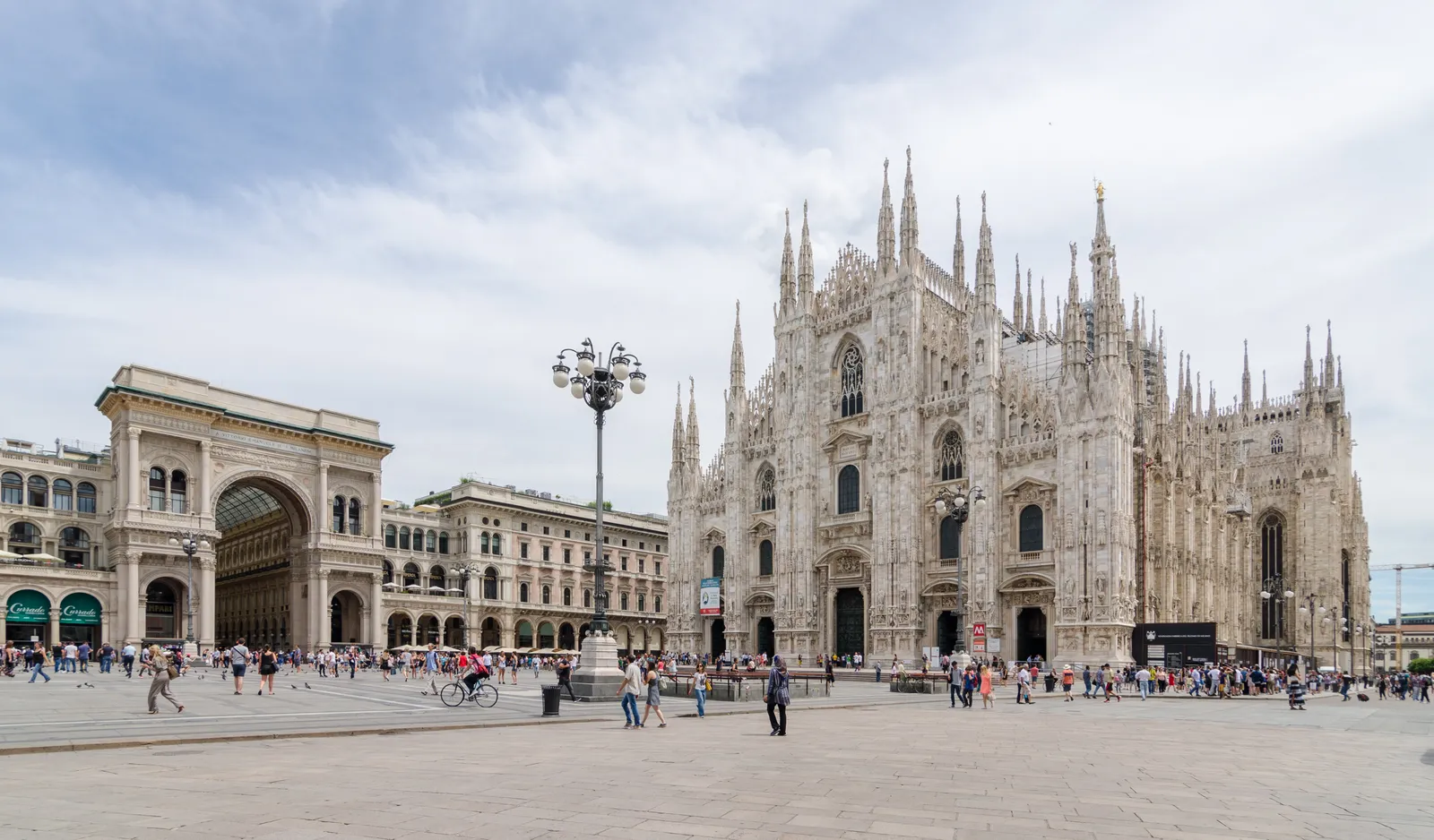 Milan Cathedral's white marble spires rising over Piazza del Duomo, with the Galleria Vittorio Emanuele II entrance arch to the left