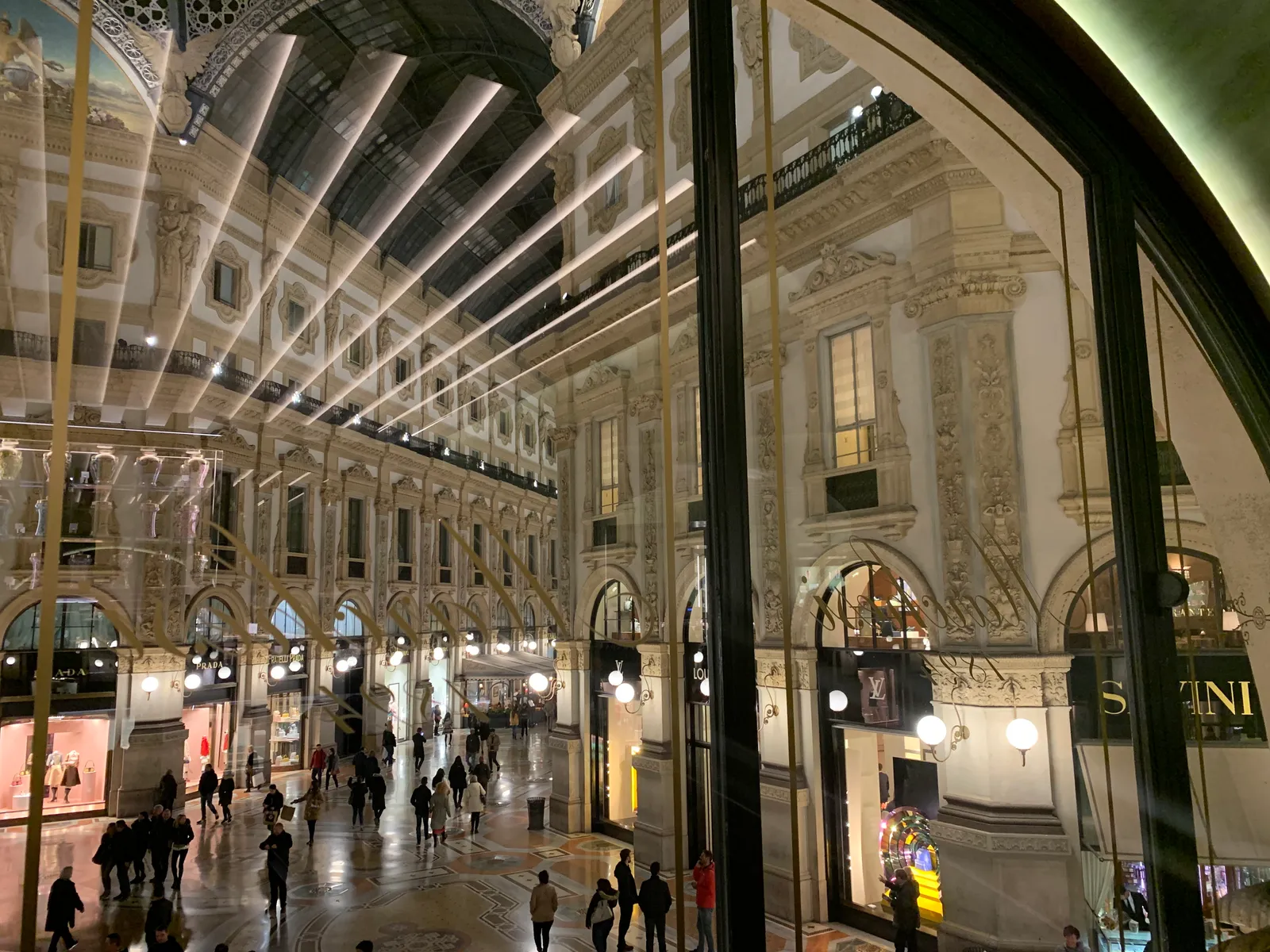 The glass-vaulted arcade of the Galleria Vittorio Emanuele II in Milan, lined with shops and full of evening foot traffic