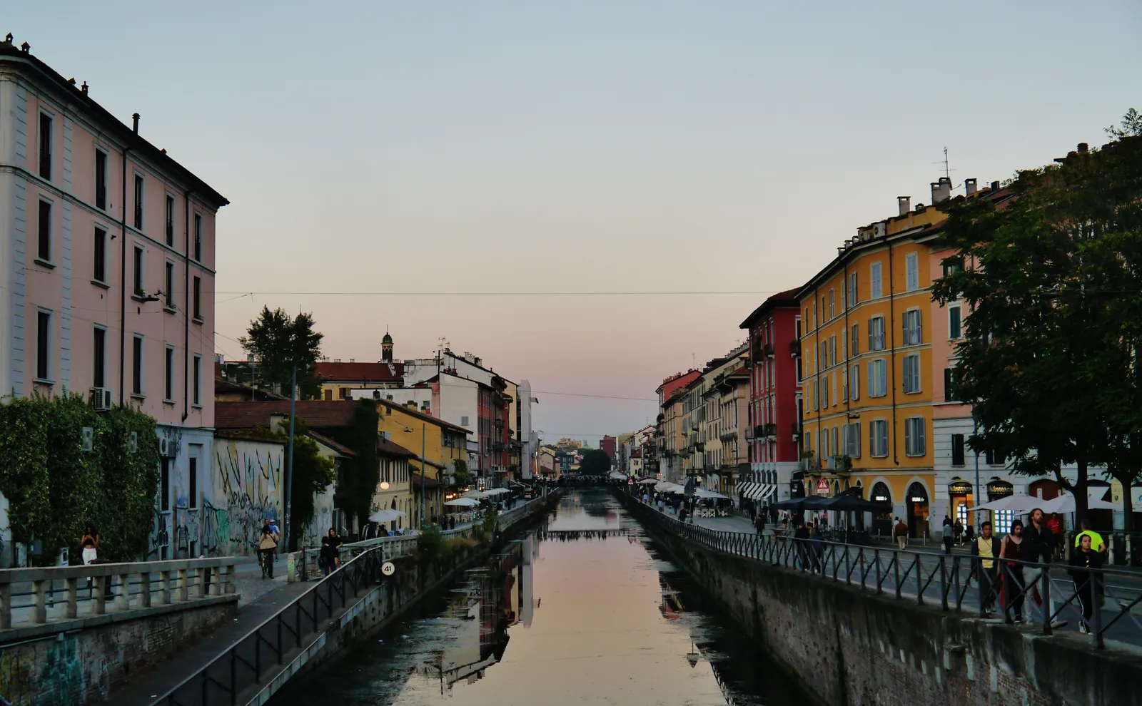 The Naviglio Grande canal in Milan at dusk, lined with colorful buildings and waterside bars