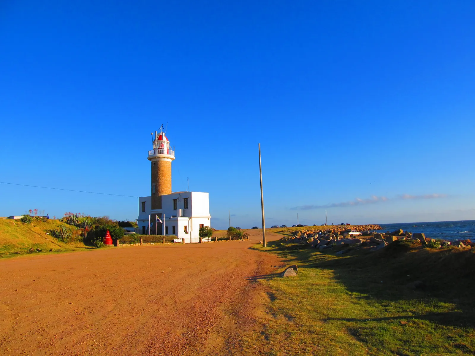 The Punta Carretas lighthouse in Montevideo, a banded brick tower on a low white building, standing on a rocky headland above the Río de la Plata under a deep blue sky