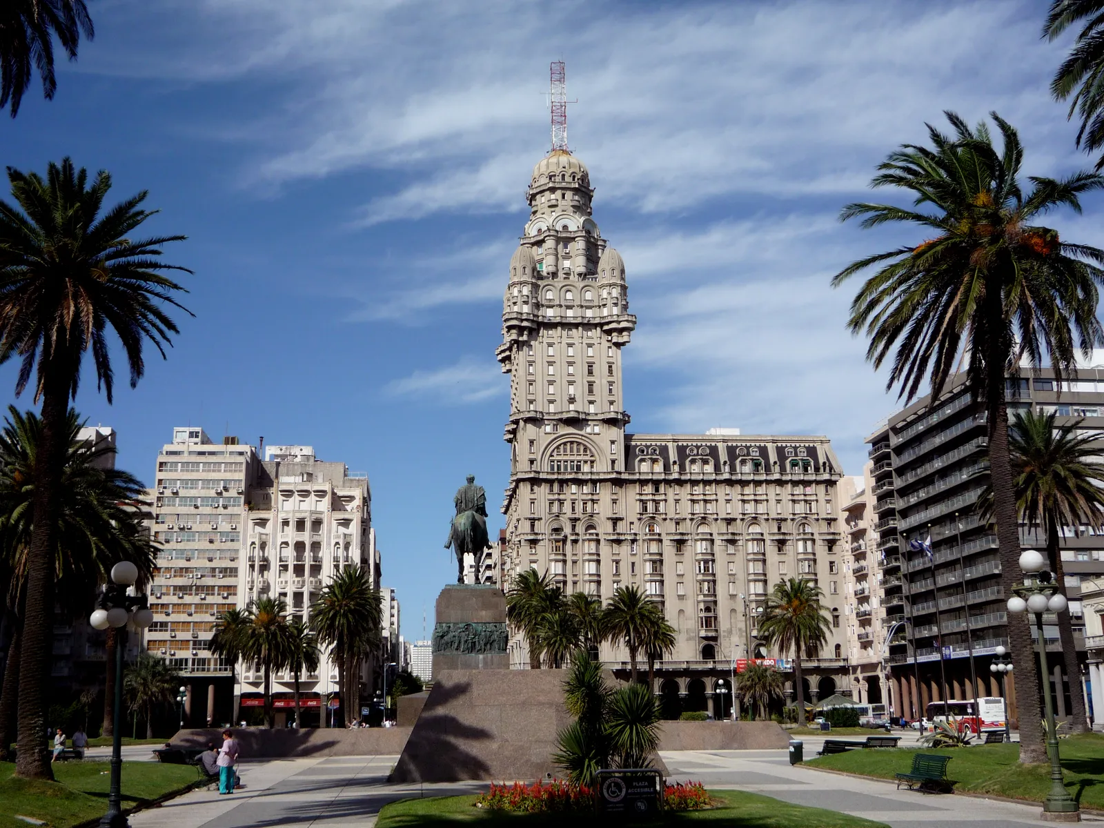 Plaza Independencia in Montevideo, with the bronze equestrian statue of José Gervasio Artigas on its granite base in the foreground and the turreted tower of Palacio Salvo rising behind it between palm trees