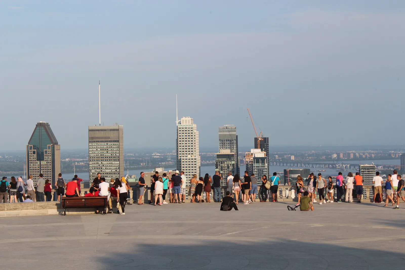 The wide stone terrace of the Kondiaronk Belvedere on Mount Royal, people lined along its balustrade with the downtown Montreal towers spread out below