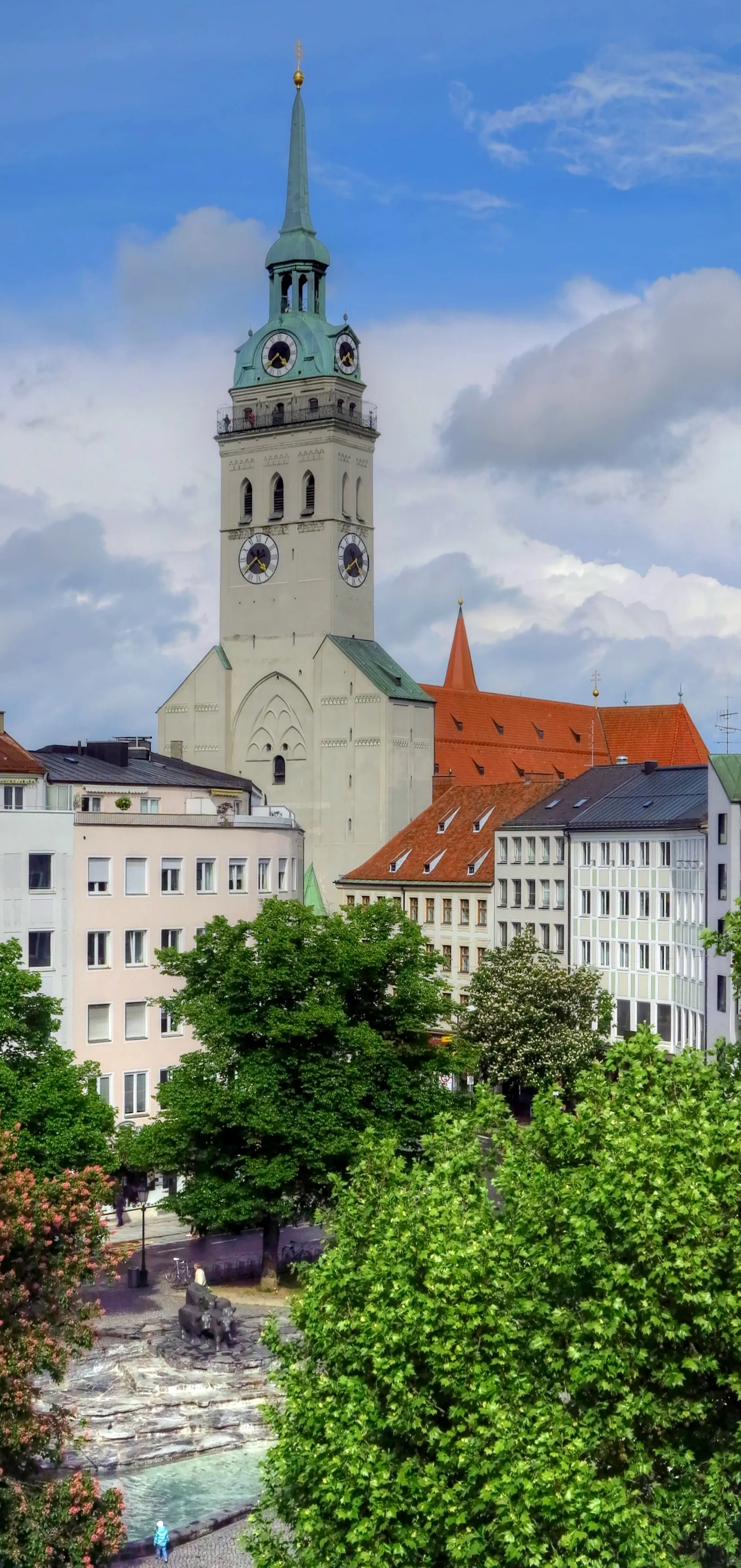 The tower of Alter Peter, St. Peter's Church in Munich, rising over the surrounding rooftops with its clock face and green spire clearly visible against the sky