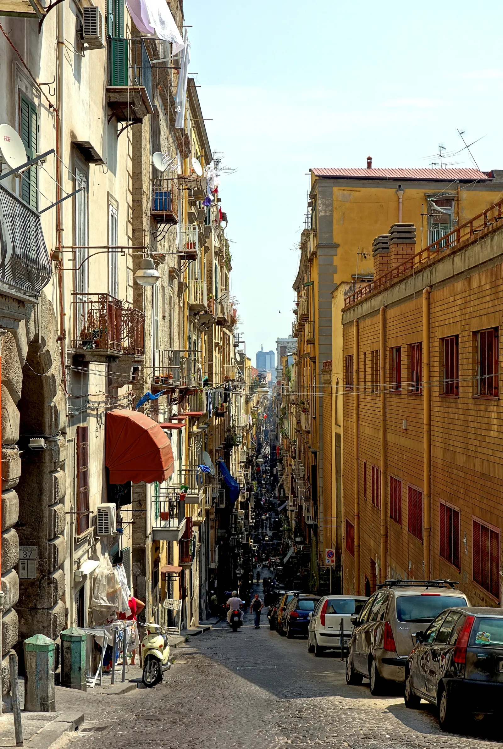 A narrow street in Naples' Spaccanapoli district lined with tall buildings, balconies, and laundry lines