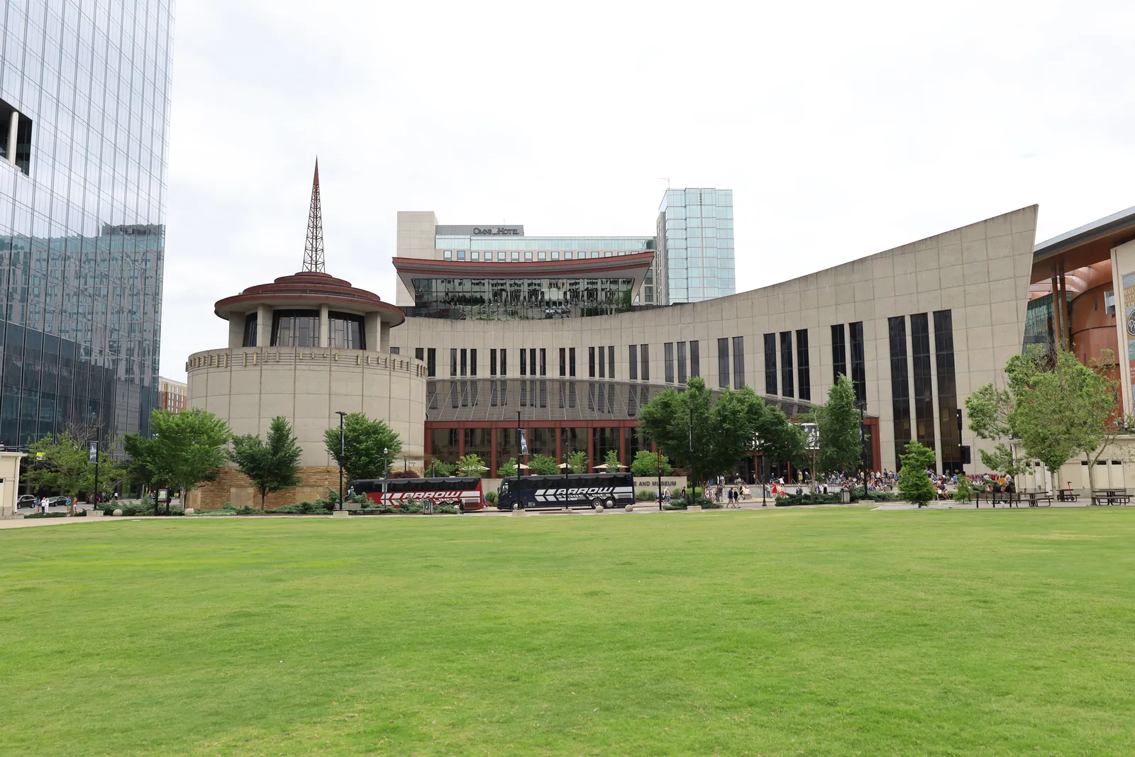 The Country Music Hall of Fame and Museum in Nashville seen across its lawn, a long curving stone wall of narrow windows running up to the round rotunda drum and its diamond-shaped radio tower