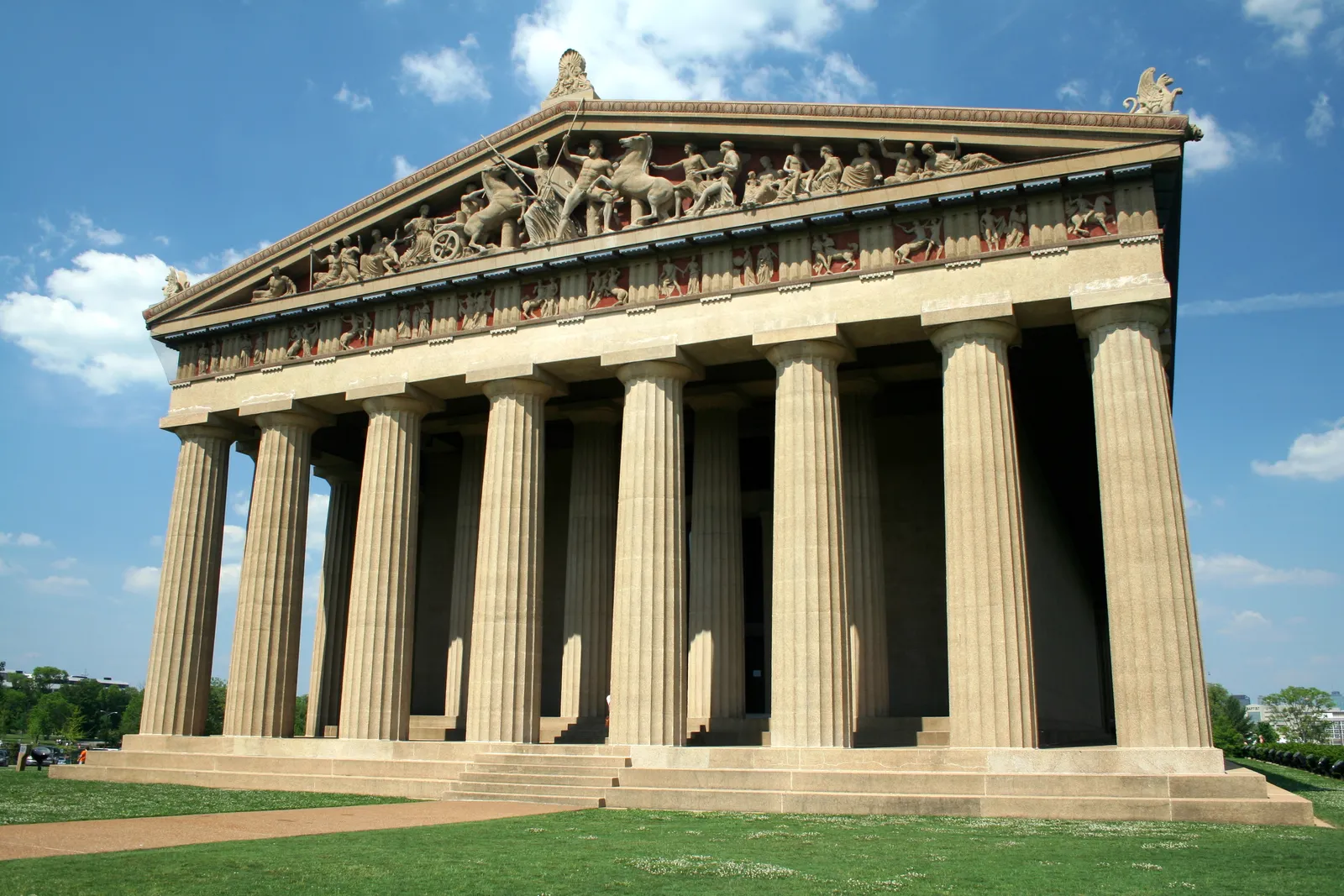 The full-size Parthenon replica in Centennial Park, Nashville, its Doric colonnade and carved pediment sculptures lit by sun against a blue sky