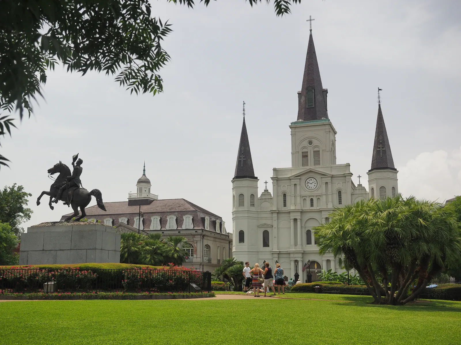St. Louis Cathedral seen across the lawn of Jackson Square in New Orleans, its three dark spires above a white facade, with the bronze equestrian statue of Andrew Jackson on the left