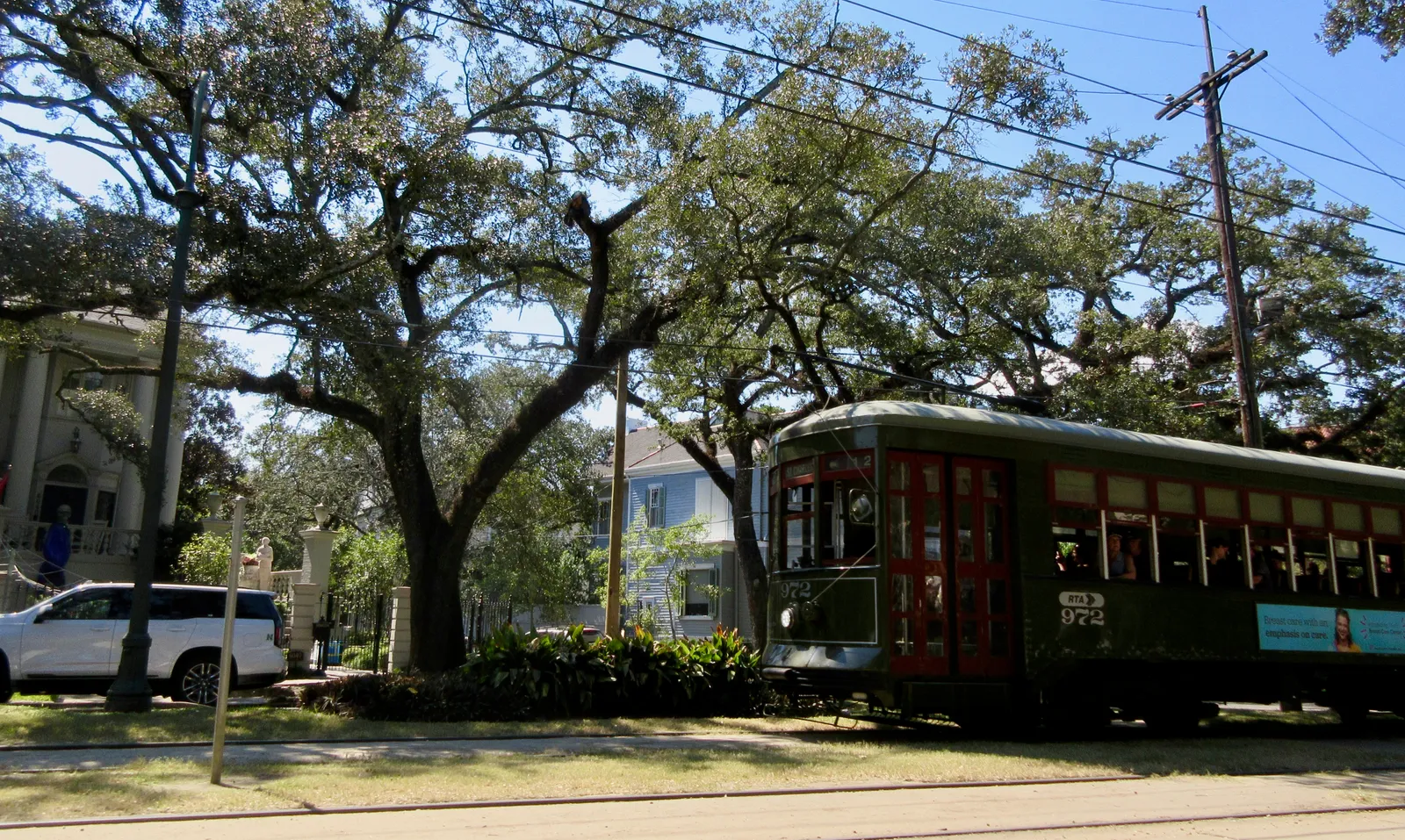 A dark green wooden streetcar running along the grass neutral ground of St. Charles Avenue in New Orleans under a canopy of live oaks