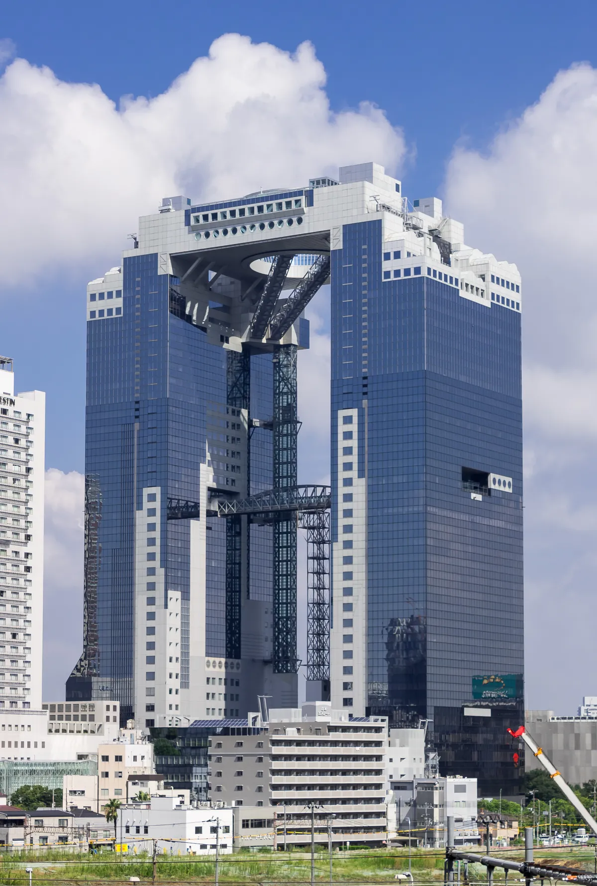The Umeda Sky Building in Osaka, two dark glass towers joined at the top by a wide platform with a circular opening cut through it, and a pair of enclosed escalator tubes crossing the open gap between the towers below