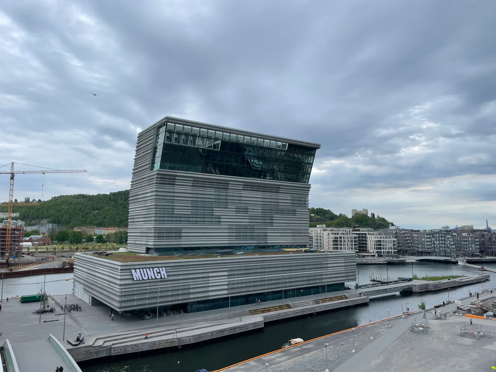 The MUNCH museum on the Oslo waterfront, a tall grey ribbed tower whose upper section leans out over the harbour, with the museum's name lit up on the low block at its base