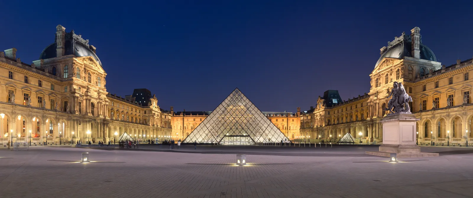 The illuminated glass pyramid in the Louvre's Cour Napoléon at night, flanked by the museum's stone wings