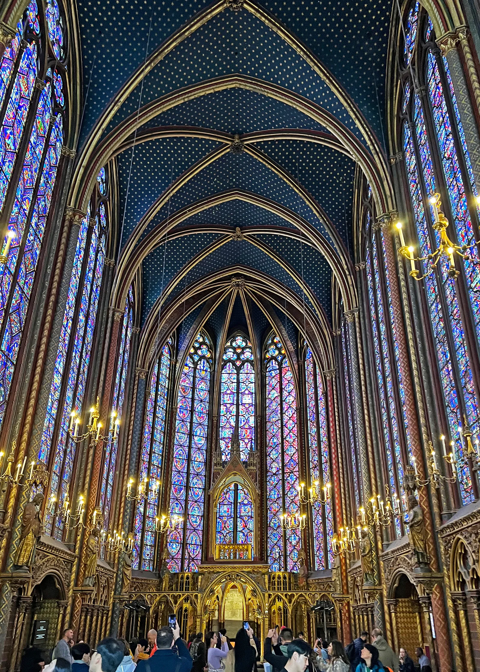 The upper chapel of the Sainte-Chapelle in Paris, its walls made almost entirely of tall stained-glass lancet windows under a blue vault painted with gold stars