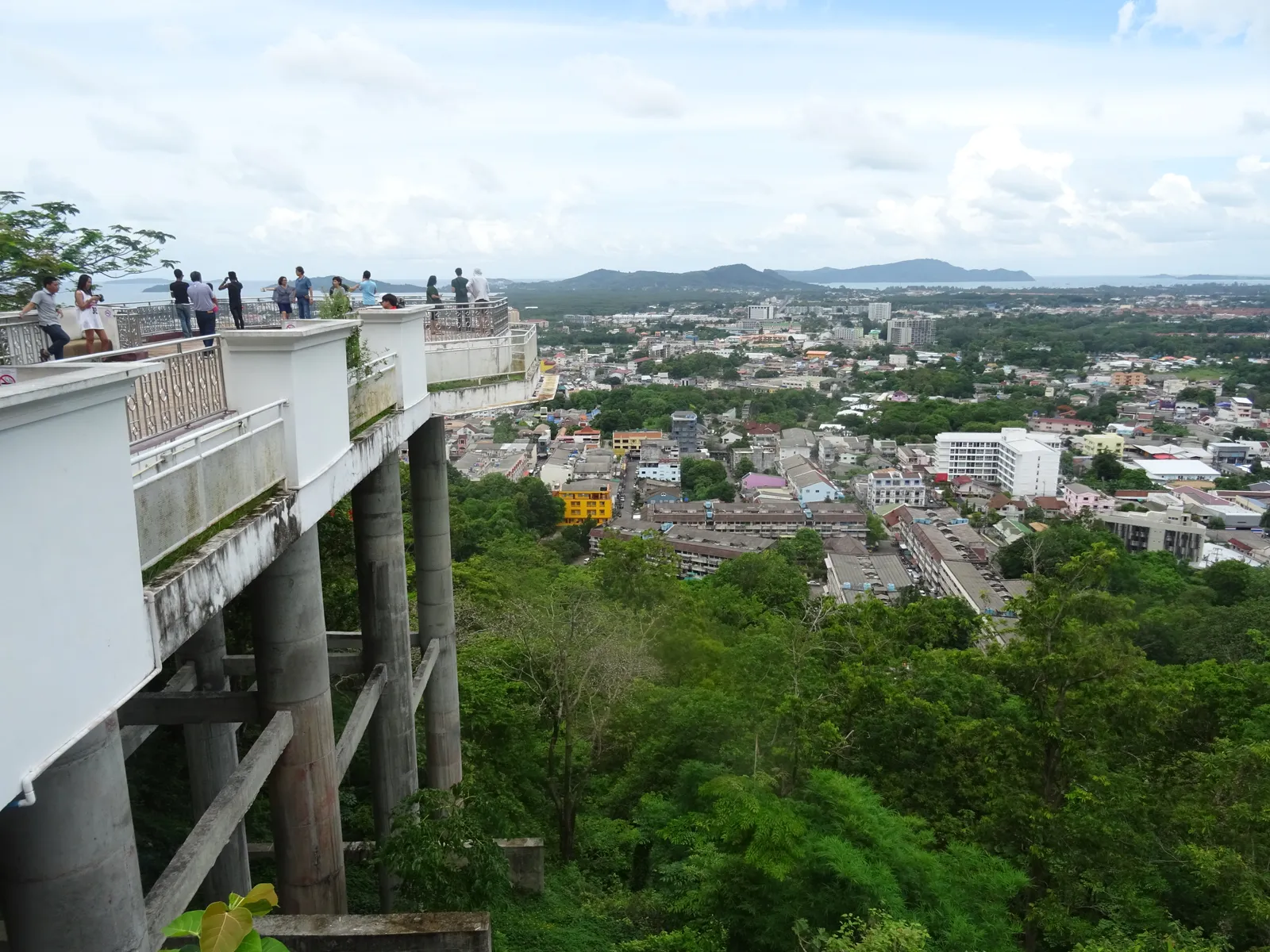 The concrete viewing terrace on stilts at the top of Khao Rang in Phuket, a handful of people at the railing looking out over the low rooftops of Phuket Town to hills and the bay beyond