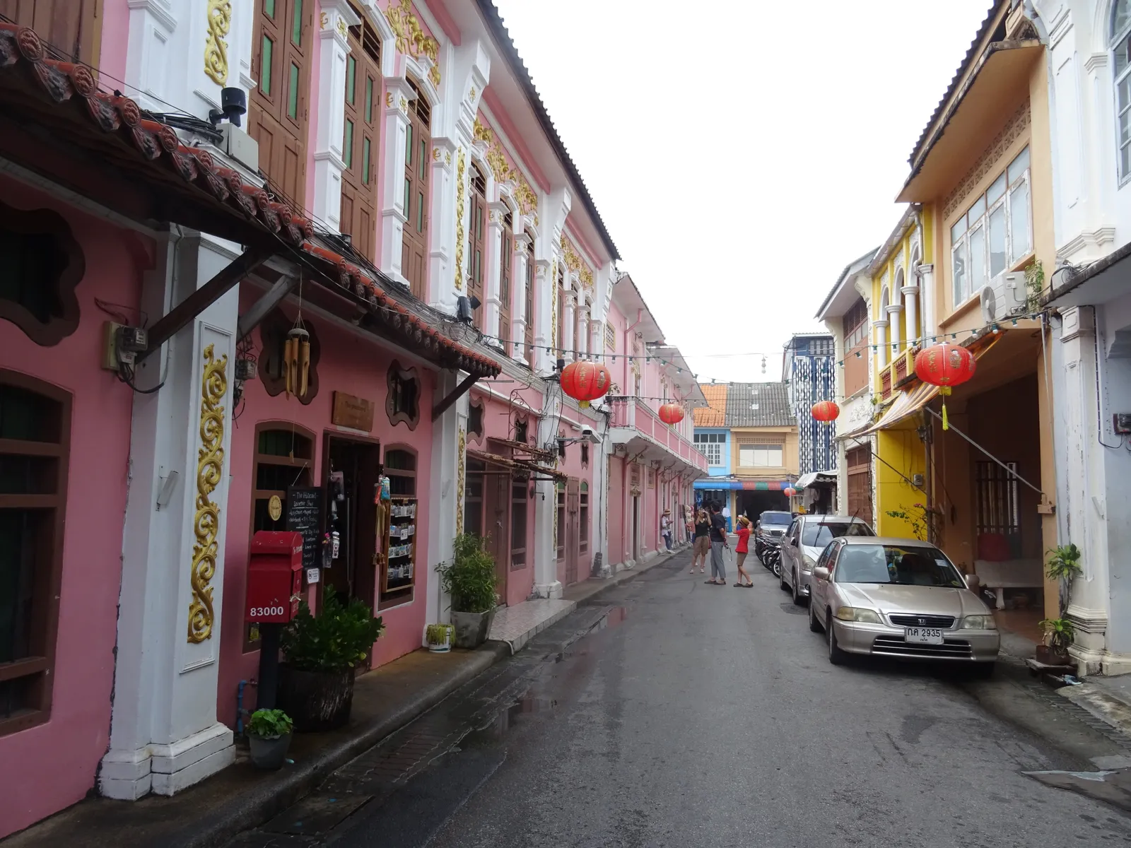 Soi Romanee in Phuket Town, a narrow lane of pink and yellow shophouses with red lanterns hung under their eaves and a few cars parked along one side
