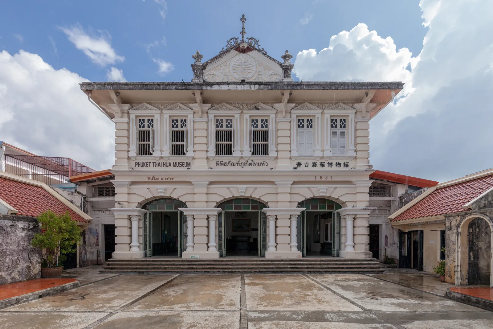 The white facade of the Phuket Thaihua Museum, a symmetrical two-storey mansion with arched ground-floor openings, paired columns and a crested gable, fronted by a paved forecourt