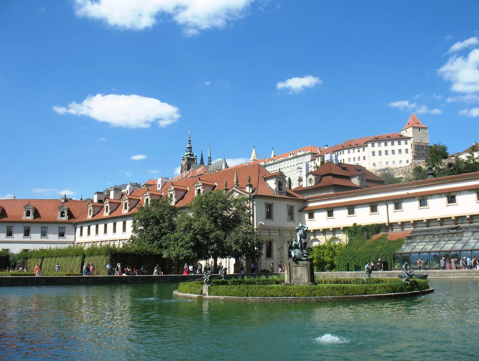 The Wallenstein Garden in Prague, with a carp pond and bronze fountain in the foreground, clipped hedges and the long Baroque riding hall behind, and Prague Castle on the wooded hill above