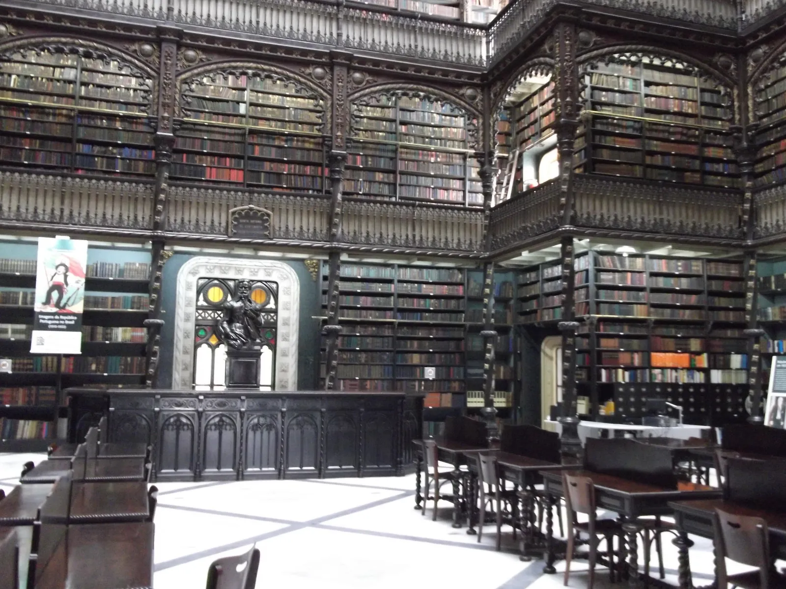 The reading room of the Royal Portuguese Cabinet of Reading in Rio de Janeiro, three storeys of carved dark wood galleries packed with books on every wall, with wooden reading tables and chairs on the pale floor below