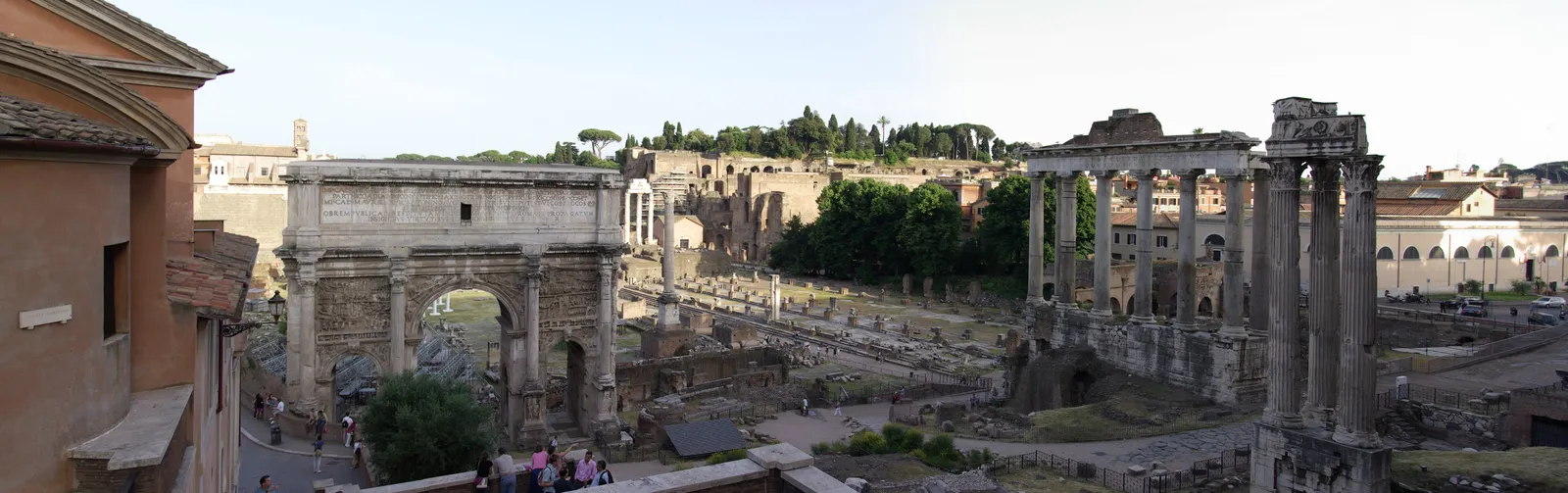 A wide view down into the Roman Forum from above, the Arch of Septimius Severus on the left, the standing columns of the Temple of Saturn to the right, and the excavated ruins of the old civic square between them