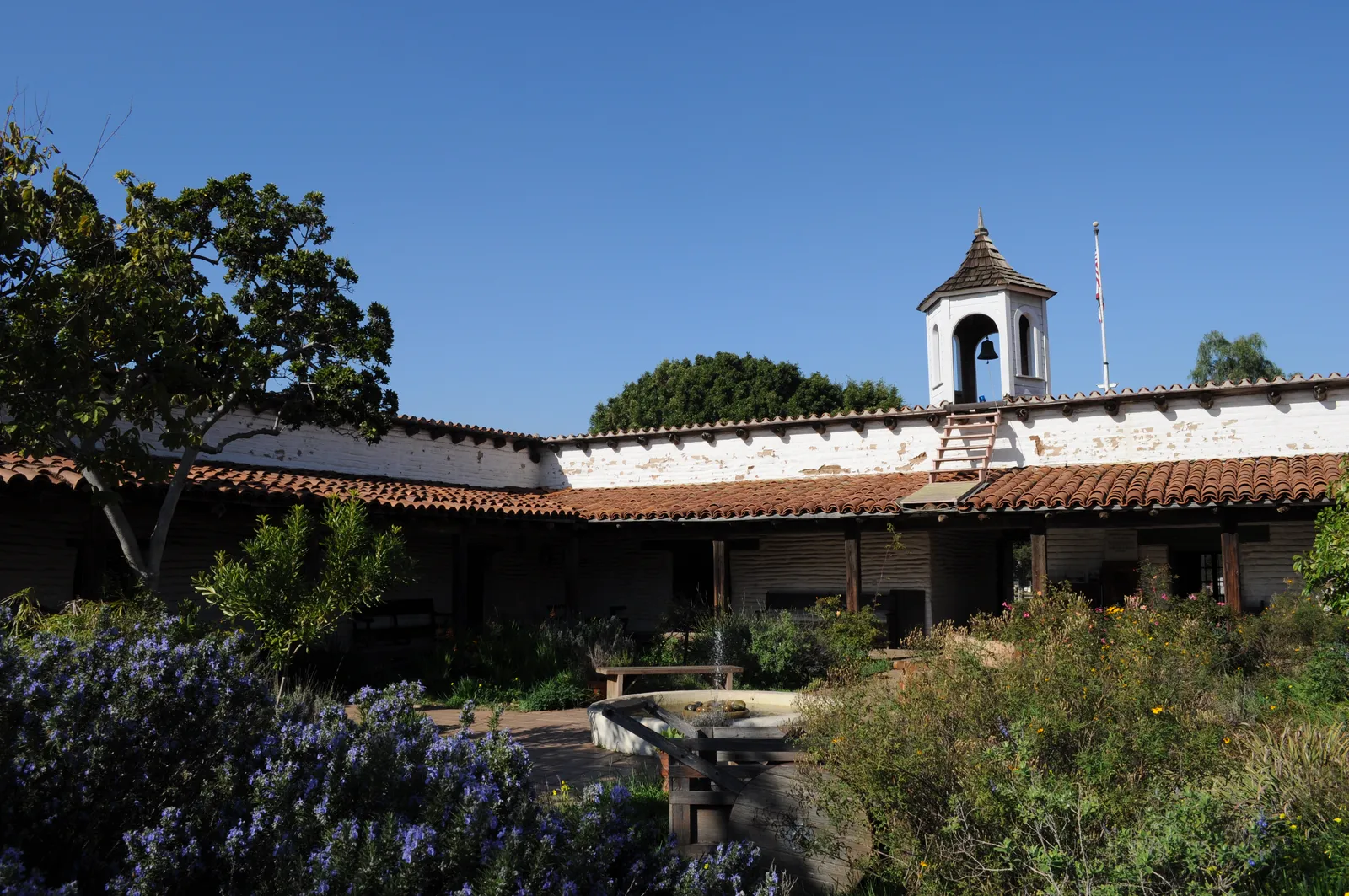 The whitewashed adobe walls, tiled roof and white bell tower of Casa de Estudillo seen from its planted inner courtyard in Old Town San Diego