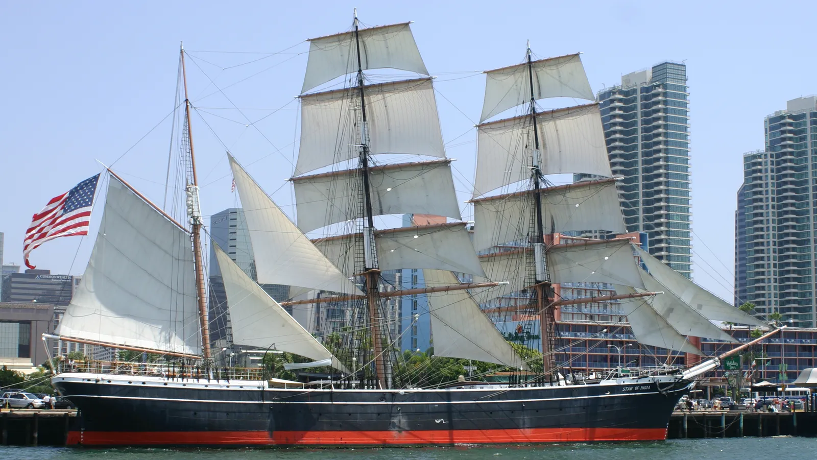 The iron sailing ship Star of India with her sails set on San Diego Bay, downtown apartment towers behind her on Harbor Drive