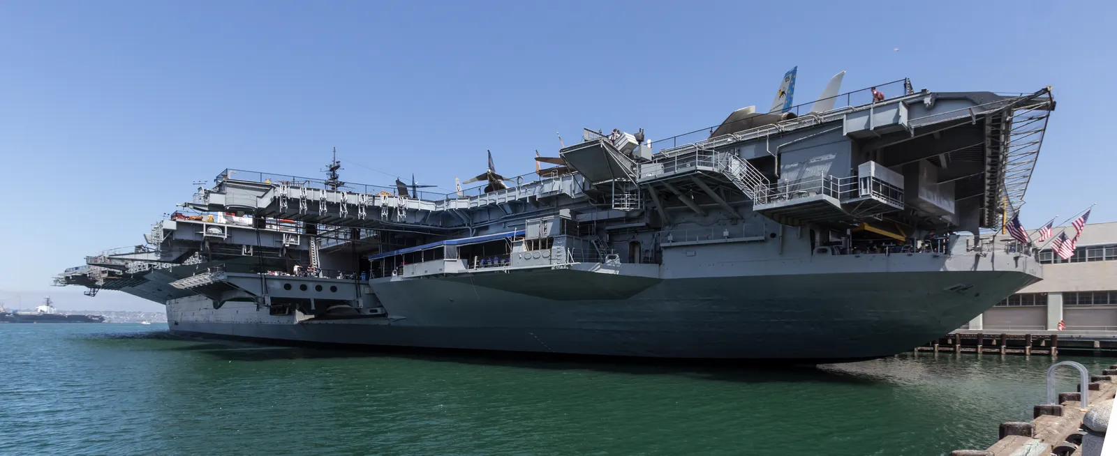 The aircraft carrier USS Midway moored alongside Navy Pier in San Diego, its flight deck lined with parked aircraft and the island superstructure rising above