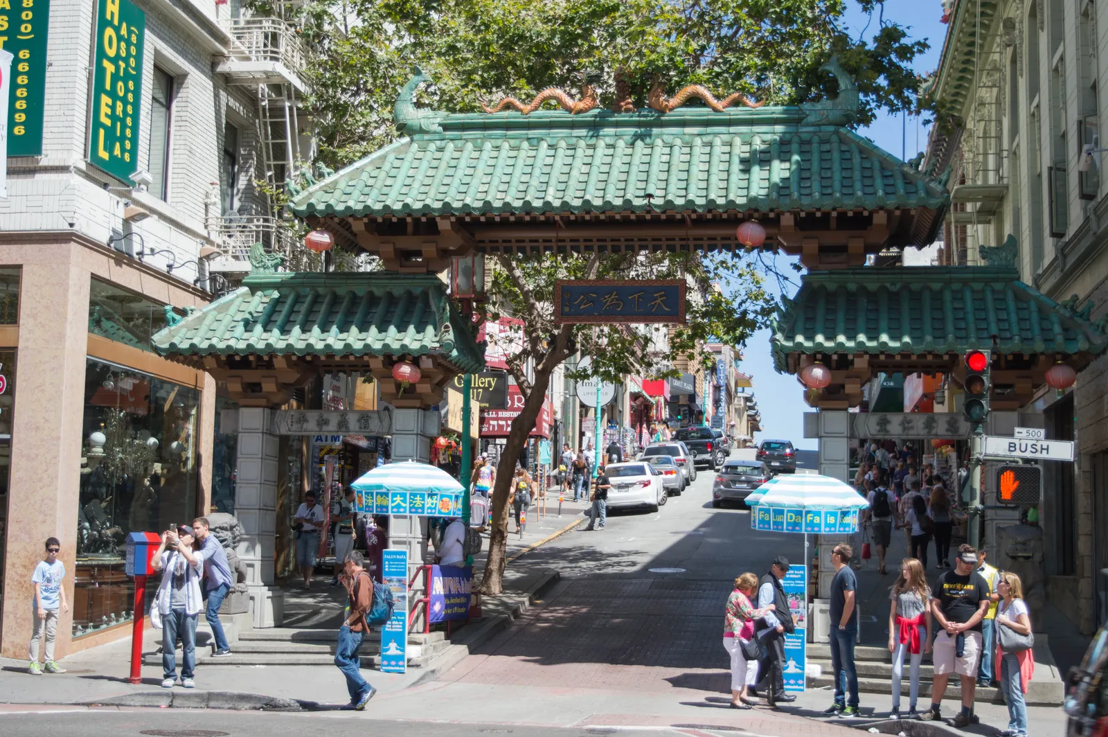 The Dragon Gate over Grant Avenue in San Francisco, a three-arched gateway with green tiled roofs and red lanterns, with shops and pedestrians on the street running away behind it