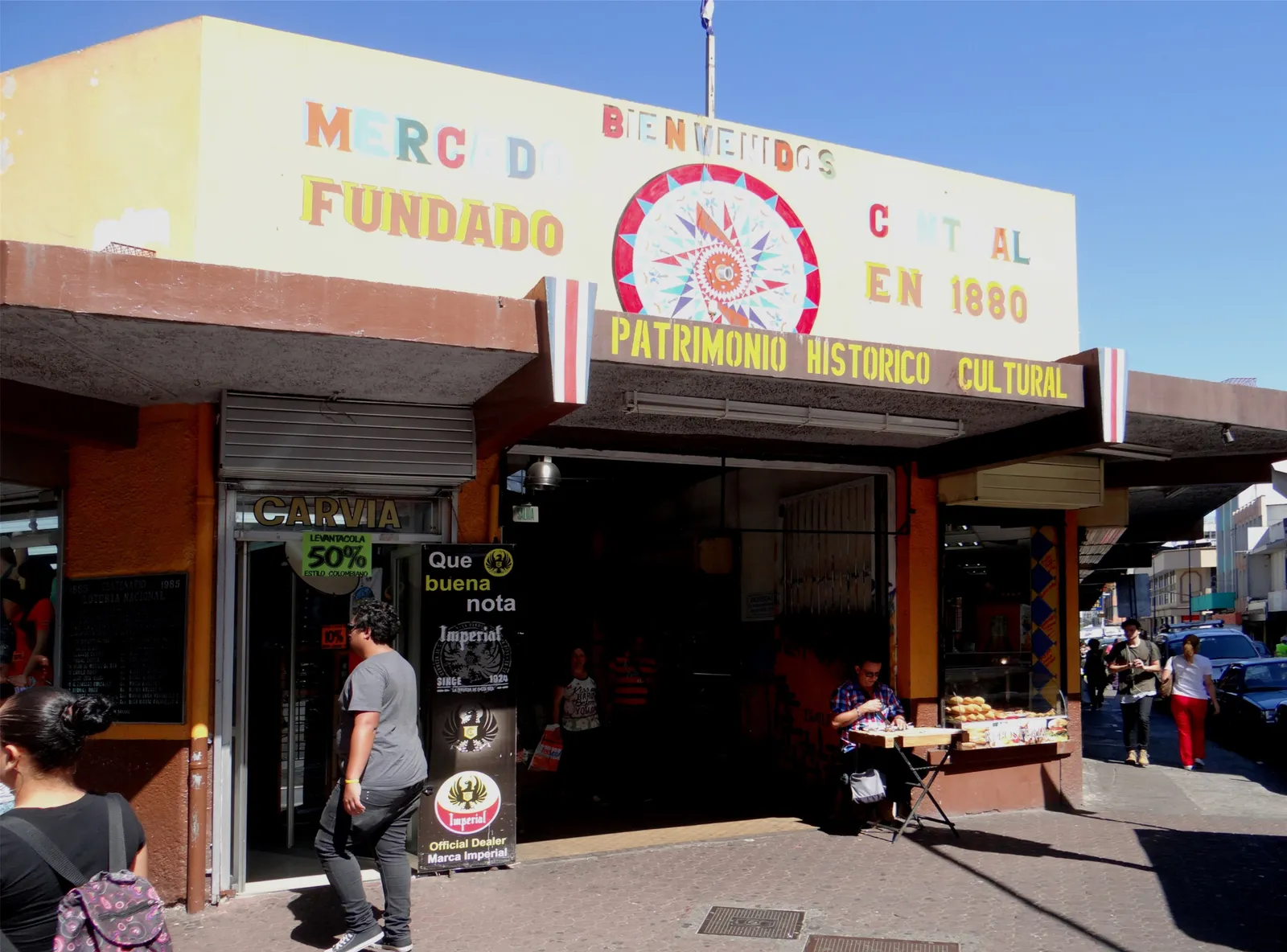 The painted sign over an entrance to San Jose's central market, reading Mercado Central, founded in 1880, historic cultural heritage, with shoppers passing underneath