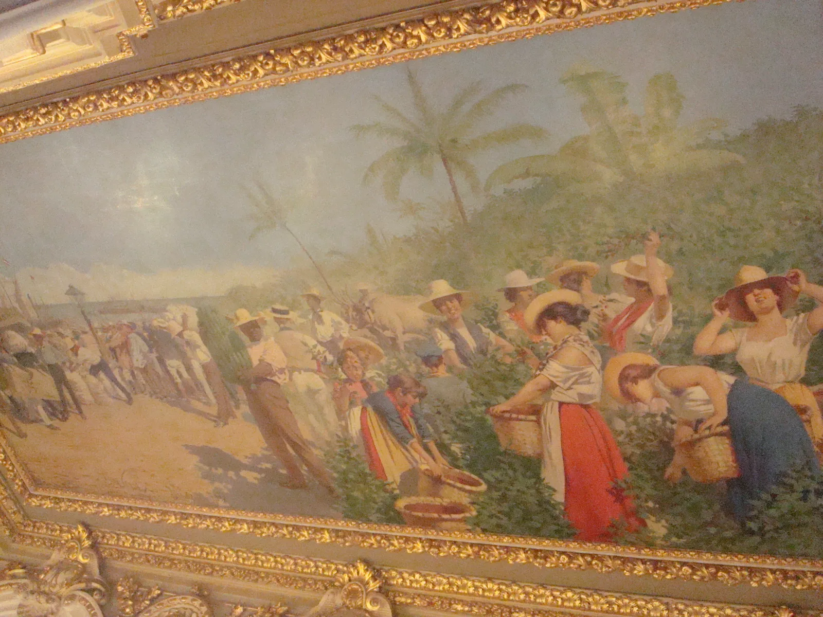 The gilt-framed ceiling fresco in the National Theatre's foyer showing coffee and banana pickers with baskets under palm trees, seen at an angle from below