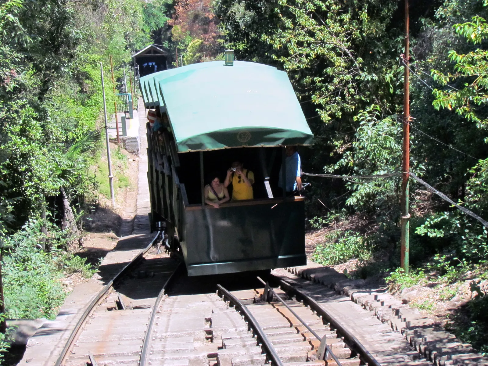 A green enclosed funicular car carrying passengers up the tree-lined track of Cerro San Cristóbal in Santiago