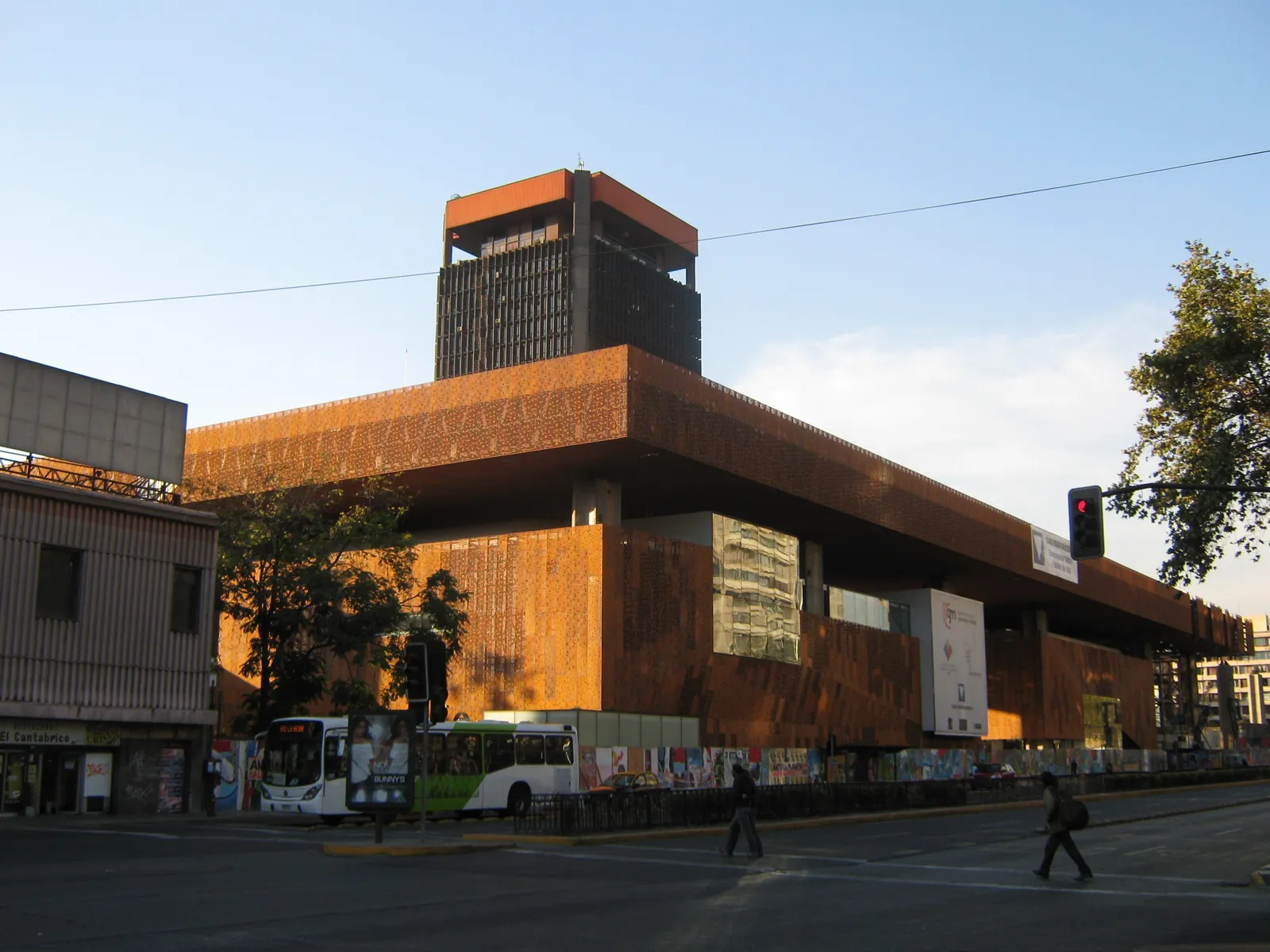 The rust-brown steel-clad Gabriela Mistral cultural centre on Santiago's Alameda, with its tall block above a long low wing, a bus passing in front