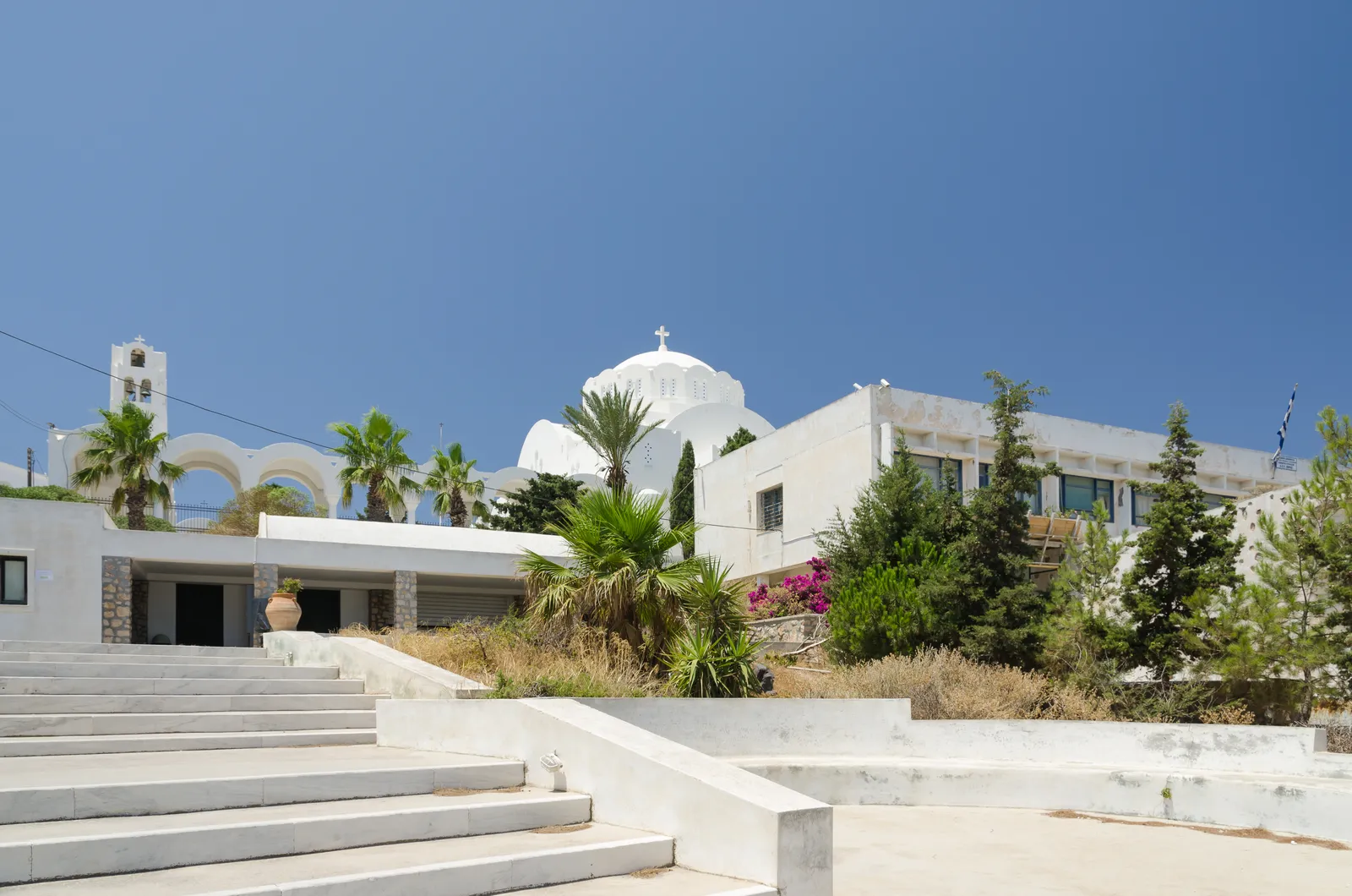 Fira's whitewashed Orthodox cathedral with its low dome and arcade of horseshoe arches, above a broad flight of white steps and a bell tower to the left