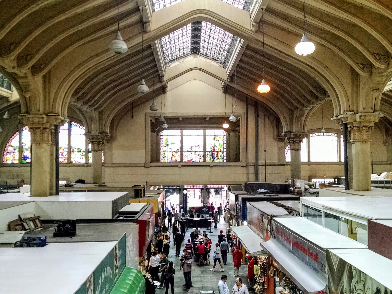 The vaulted stone interior of the Municipal Market in São Paulo, with stained-glass windows set high in the walls above ranks of food stalls and shoppers walking the aisles below